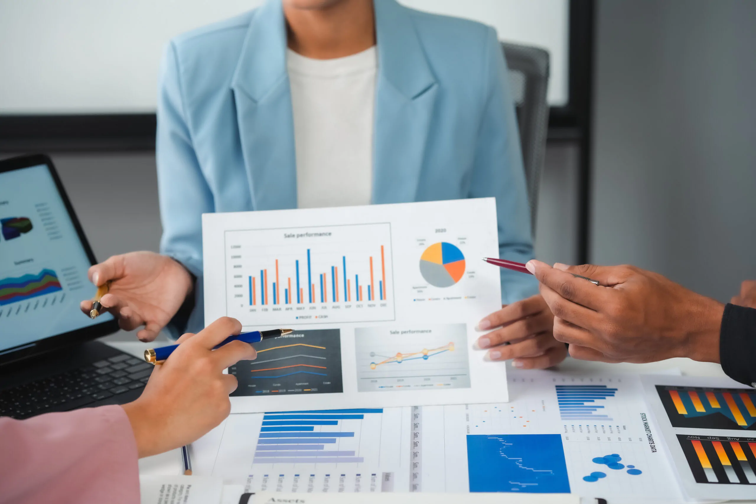 Close-up of business professionals pointing to colorful sales performance charts and data visualizations during a financial management meeting.